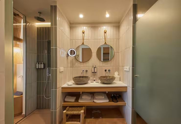 Badezimmer mit zwei Steinwaschbecken, rund aufgehängten Spiegeln und Regendusche.