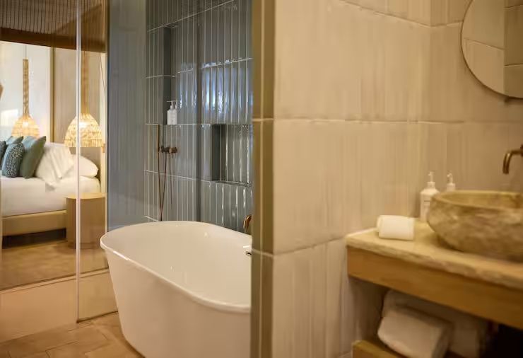 Freistehende weiße Badewanne vor einer grau gefliesten Wand im Badezimmer des Resorts.