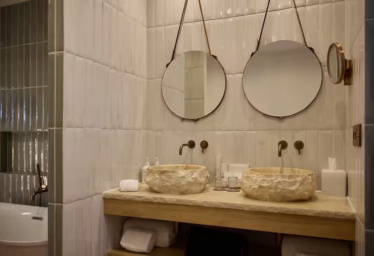 Doppelwaschtisch mit zwei Steinwaschbecken und runden Spiegeln an der hellen Wand.