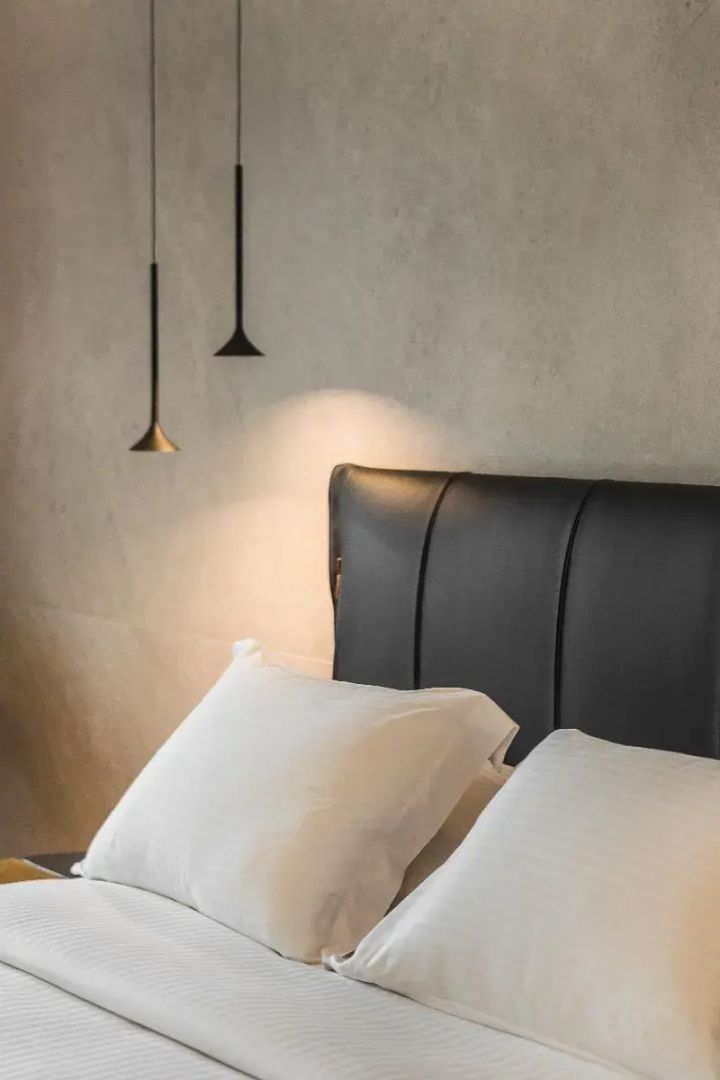 Polsterkopfteil eines Bettes mit weißen Kissen und modernen Hängeleuchten an der Wand.