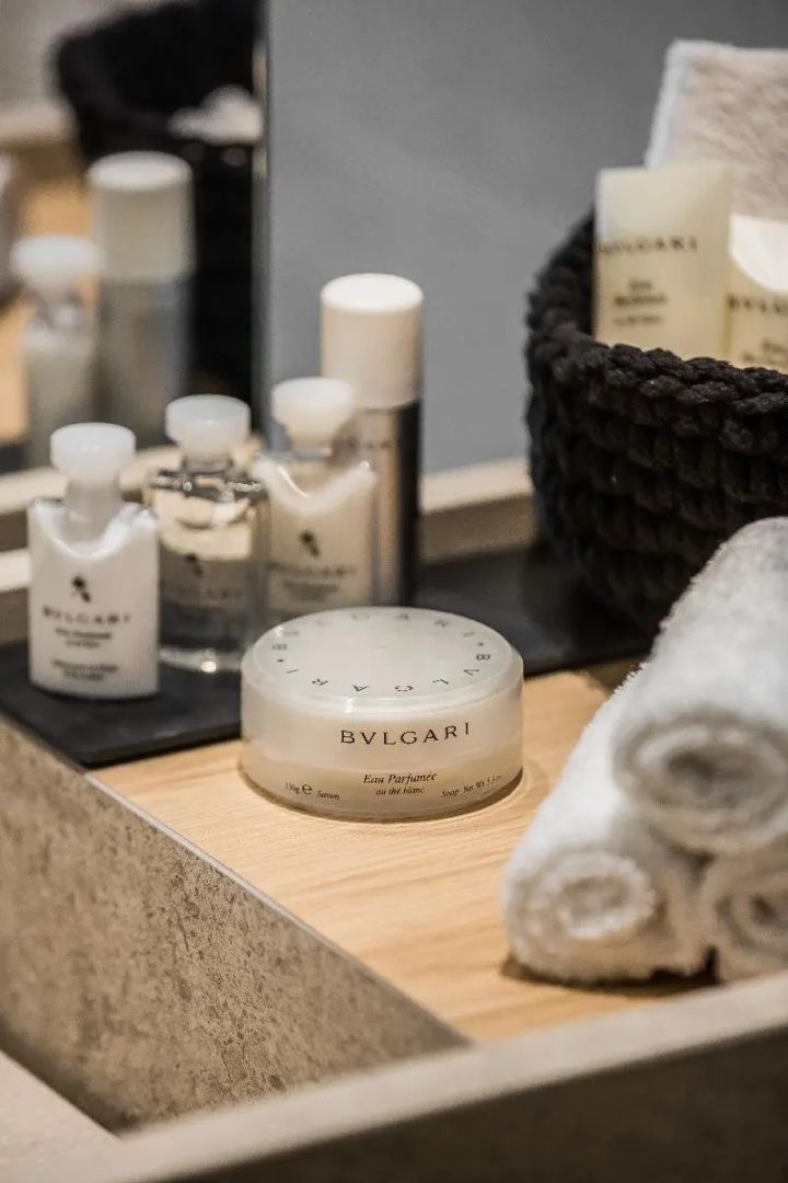 Pflegeprodukte der Marke Bvlgari und gerollte Handtücher auf einem Waschtisch im Bad.