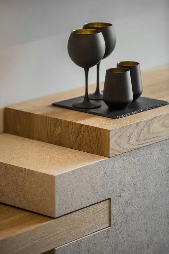 Schwarze Gläser und Becher stehen auf einer Holz- und Steinablage im Hotelzimmer.