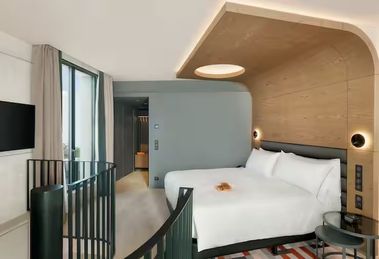 Doppelbett mit weißer Bettwäsche unter einer Holzkonstruktion in einem hellen Hotelzimmer.