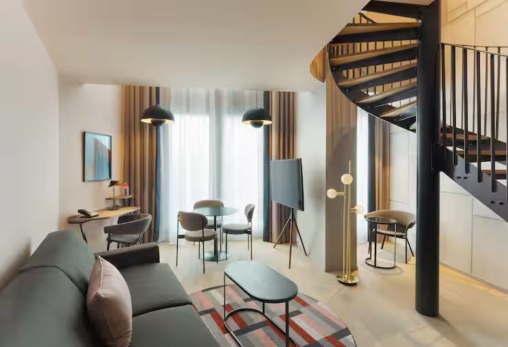 Wohnbereich einer Suite mit Sofa, Teppich, kleinem Esstisch, Fernseher und Wendeltreppe.