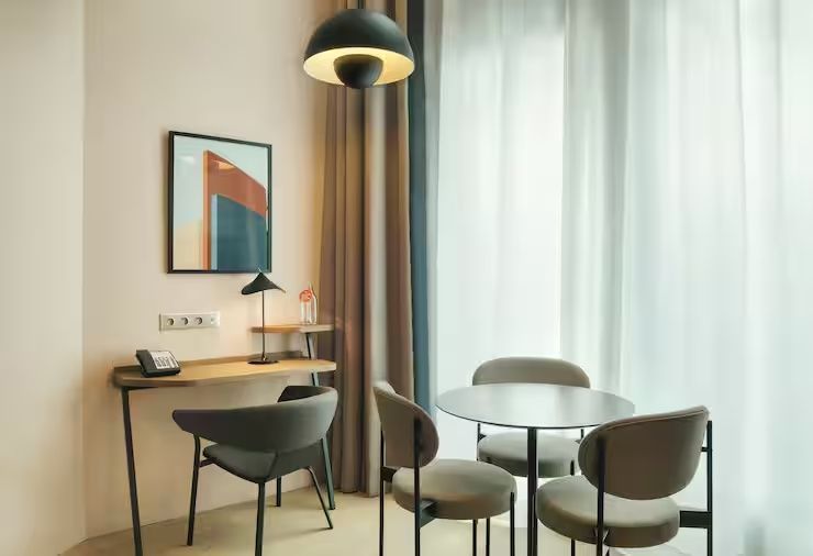Sitzbereich im Zimmer mit rundem Tisch, vier Stühlen sowie einem kleinen Wand-Schreibtisch.