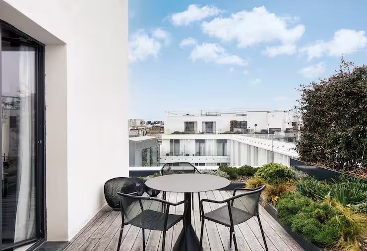 Holzterrasse mit einem schwarzen Tisch, Stühlen und Ausblick auf die Dächer der Stadt.