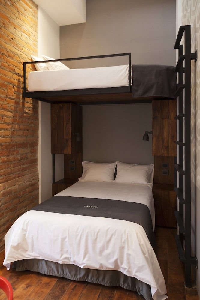 Zimmer mit Holzetagenbett neben einer Wand aus rotem Backstein und weißem Bettzeug.