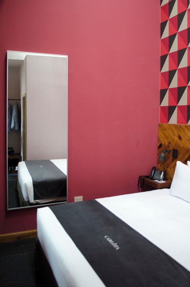 Hotelzimmer mit weißem Bett, rosa Wand, langem Wandspiegel und Kopfteil aus Holz.