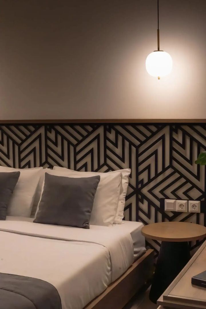 Doppelbett mit weißer Bettwäsche und auffälligem Kopfteil mit geometrischem Muster.