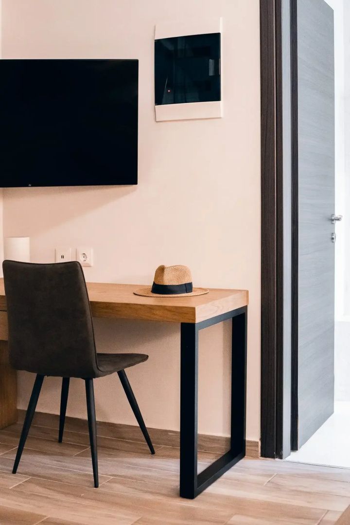 Holzschreibtisch mit dunklem Stuhl und einem Strohhut in einem modern eingerichteten Zimmer.