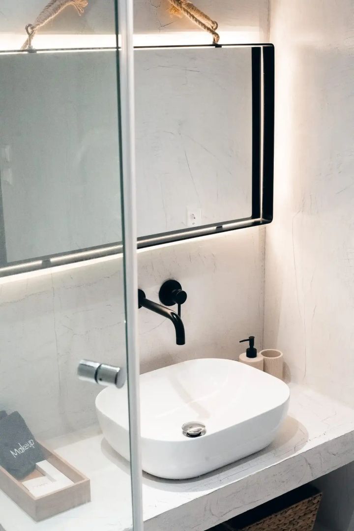 Weißes Aufsatzwaschbecken mit schwarzer Armatur und beleuchtetem Spiegel im Badezimmer.
