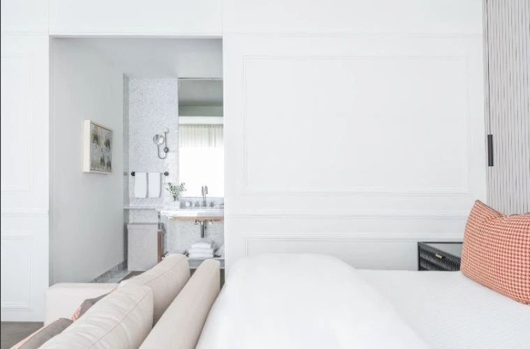 Blick vom Schlafbereich eines hell eingerichteten Hotelzimmers in das angrenzende Badezimmer.