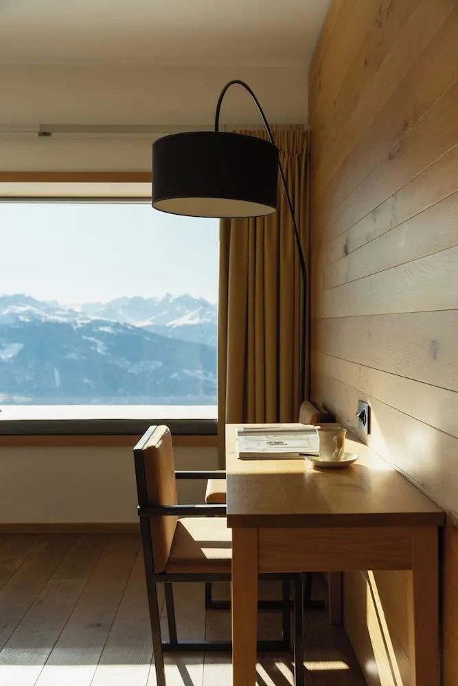 Schreibtisch aus Holz und große Fensterfront mit Blick auf verschneite Berge.