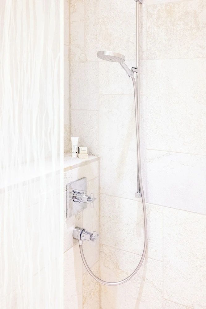 Modernes Duschbad mit hellen Steinfliesen, verchromter Armatur und Handbrause.