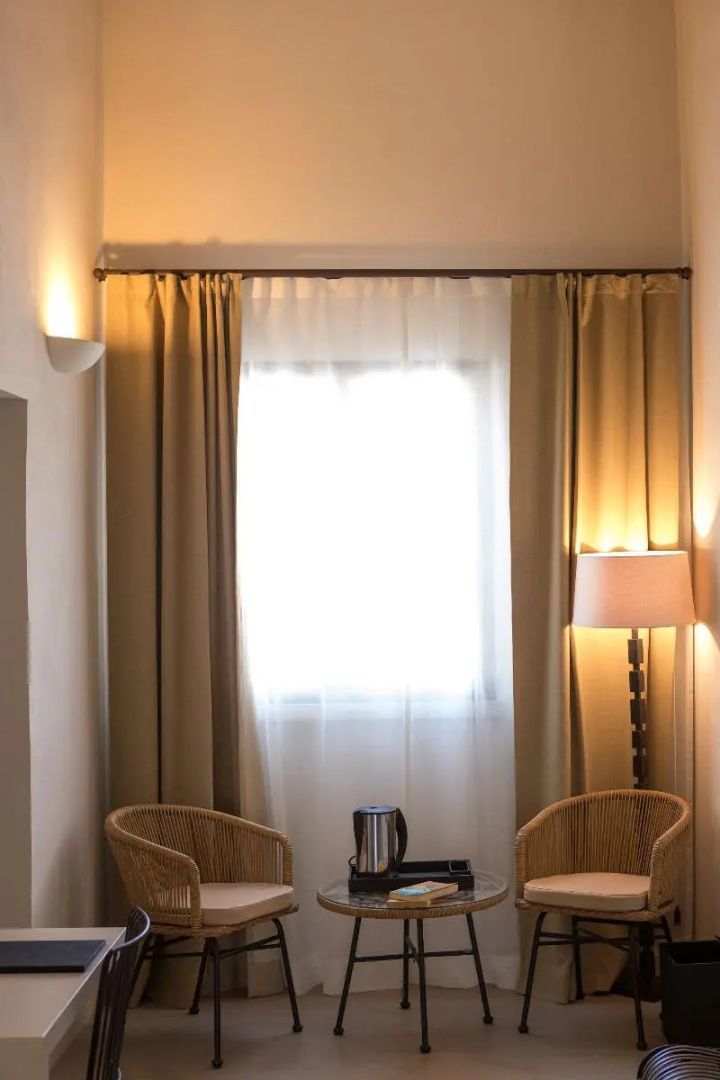 Sitzecke mit zwei Flechtstühlen, Stehlampe und Vorhängen vor dem hellen Fenster.