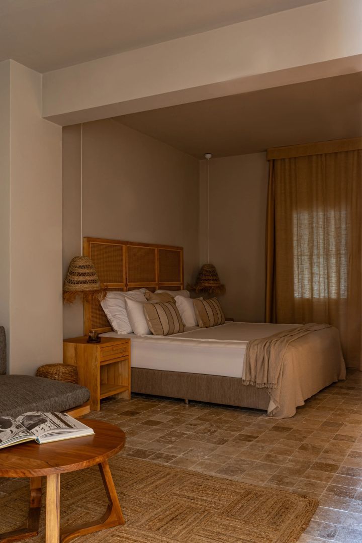 Doppelbett mit Holzkopfteil, Hängelampen aus Geflecht und Vorhang im Hotelzimmer.