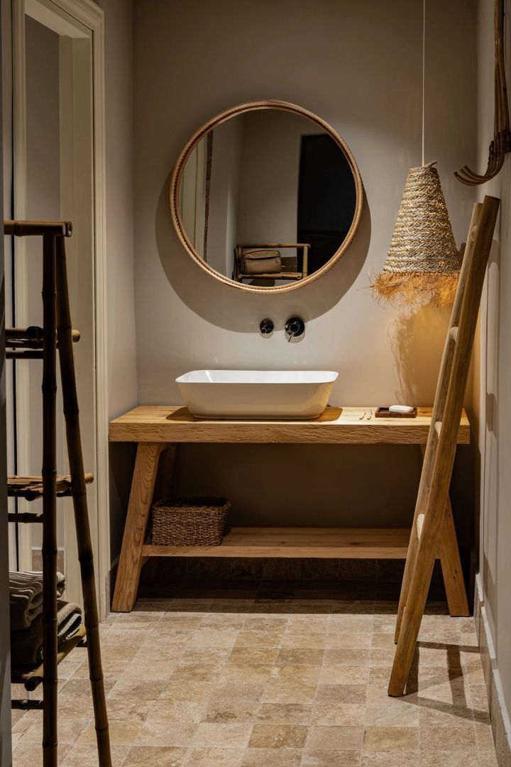 Waschbecken auf einem Holzwaschtisch mit rundem Spiegel und geflochtener Lampe.