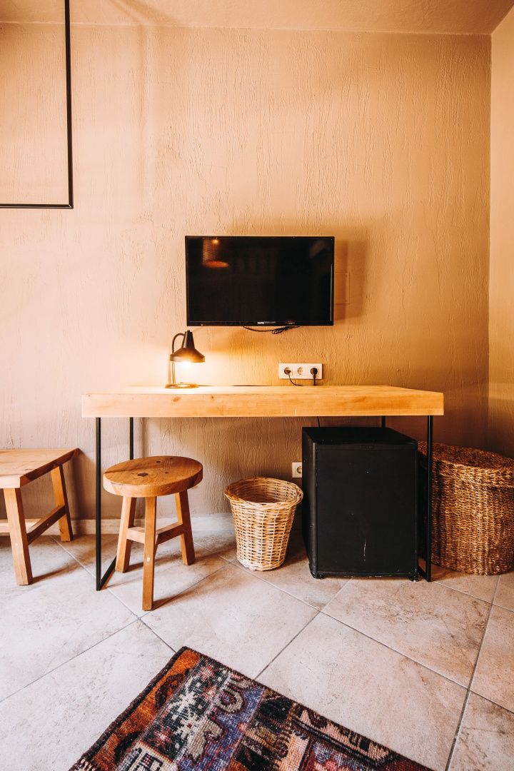 Schreibtisch aus Holz mit Stuhl, Flachbildfernseher an der Wand, Minibar und Flechtkorb.