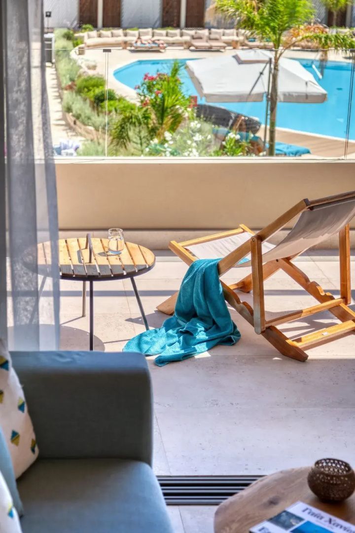 Balkon mit einem Holzliegestuhl, einem blauen Handtuch und einem kleinen runden Tisch.