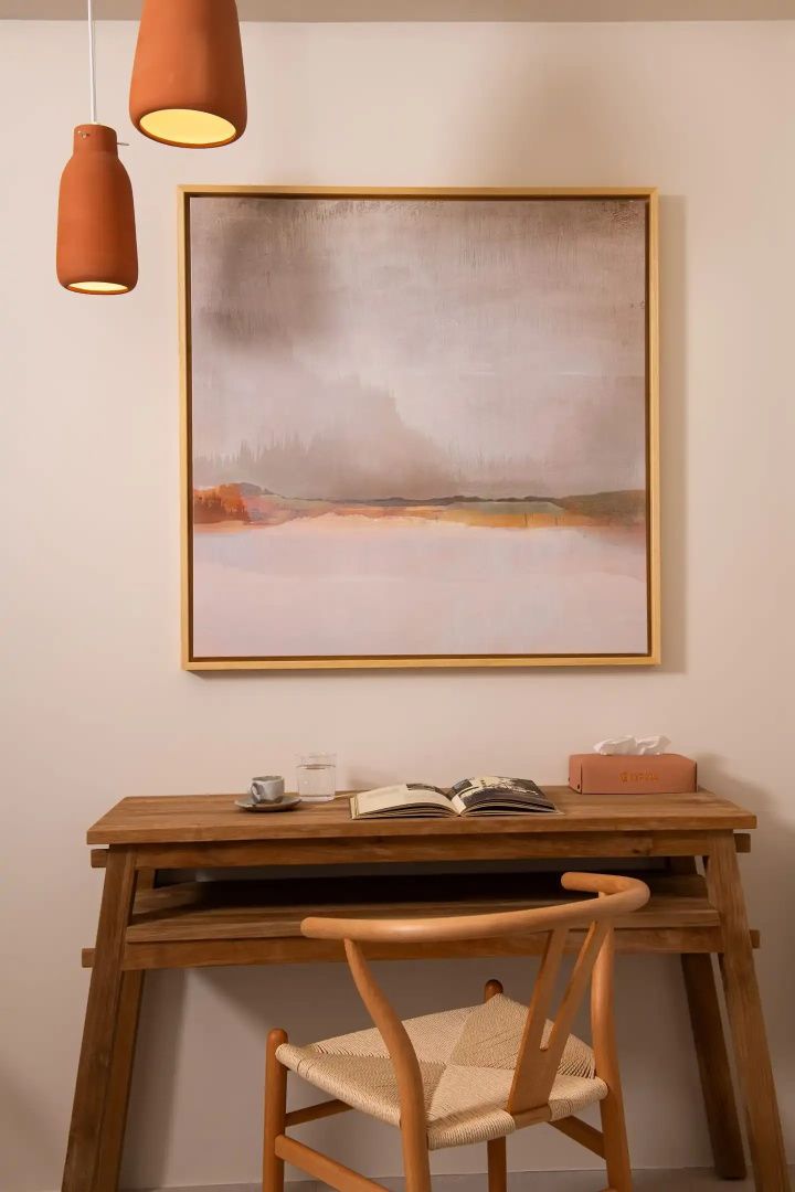 Holztisch mit aufgeschlagenem Buch und Kaffeetasse unter einem abstrakten Gemälde an der Wand.