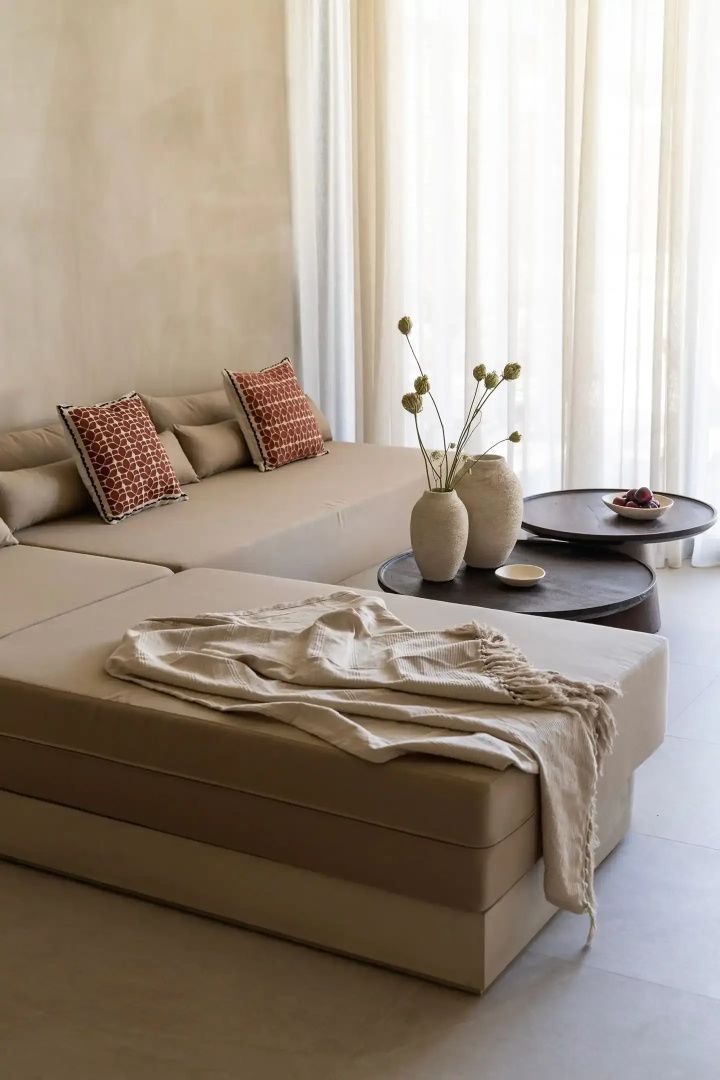 Sitzbereich mit beigefarbenem Sofa, bestickten Kissen und zwei dunklen Beistelltischen.