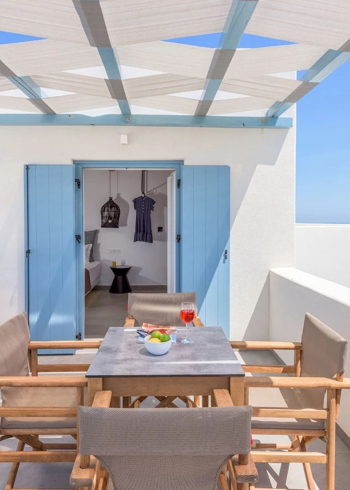 Terrasse mit Holzstühlen, einem Tisch und hellblauen Läden vor der Eingangstür.