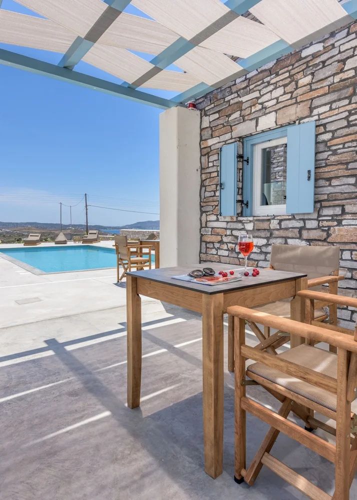 Überdachte Terrasse mit Holztisch, Stühlen und Ausblick auf den Poolbereich.