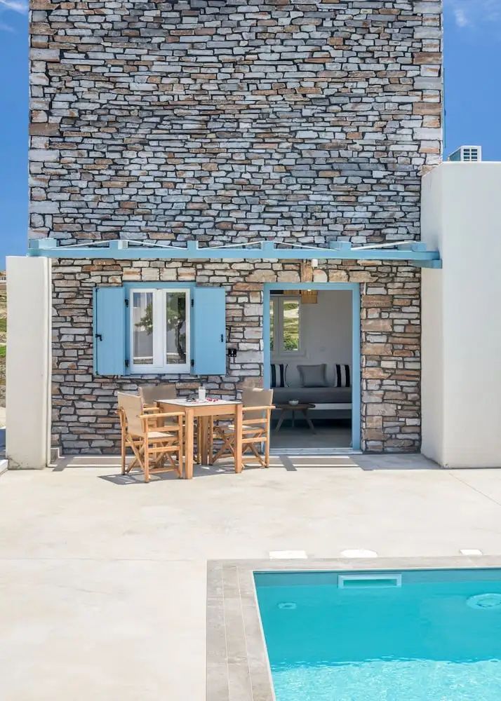 Natursteinfassade mit blauen Fensterläden, Sitzgruppe auf der Terrasse und Pool.