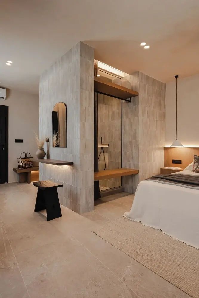 Offener Raum mit Bett, integrierter Dusche hinter einer Trennwand und kleiner Bank