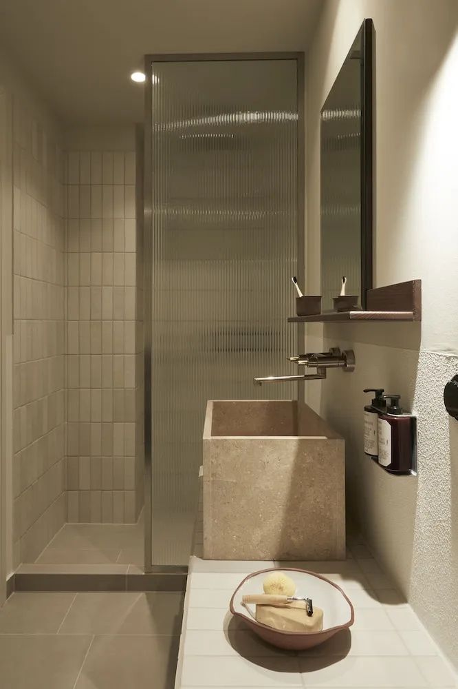 Badezimmer mit rechteckigem Waschtisch aus Stein und einer gläsernen Dusche.