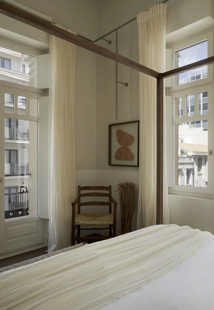 Zimmerecke mit Holzstuhl, Wandbild und großem Fenster neben einem Himmelbett.