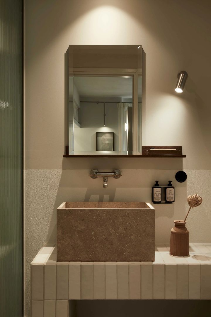 Rechteckiges Waschbecken aus Stein im Badezimmer mit Spiegel und Seifenspendern an der Wand.
