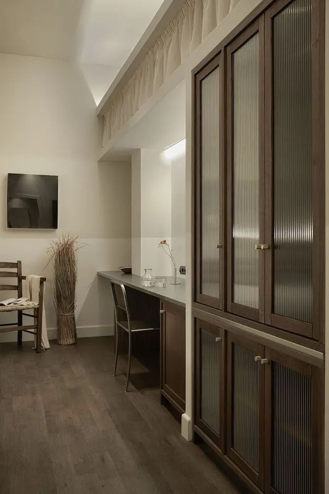 Holzschrank mit Riffelglas, Schreibtischbereich und Stuhl im Hotelzimmer.