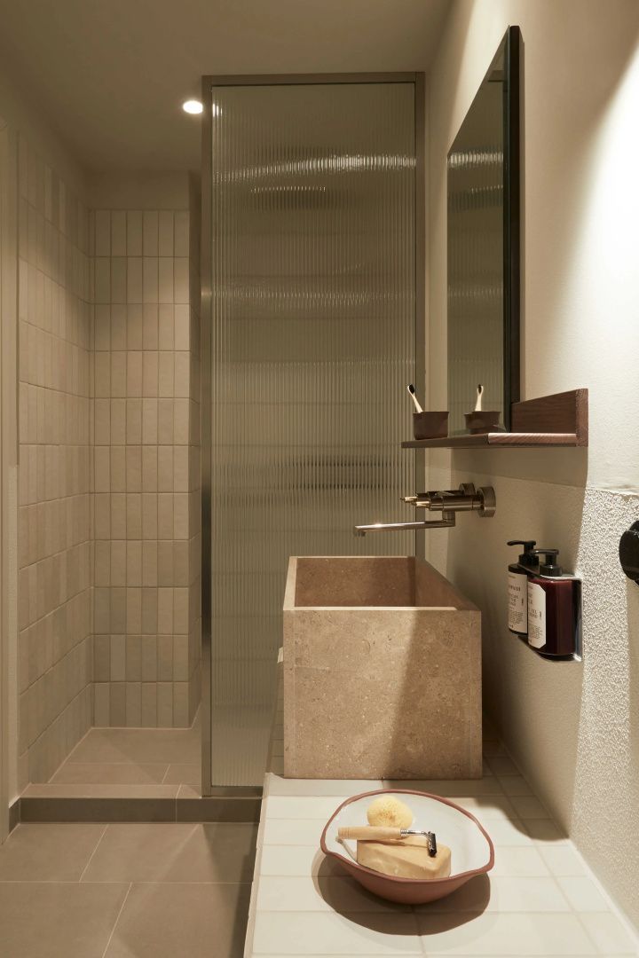 Badezimmer mit einem steinernen Waschtisch, einer Glasduschwand und hell gefliester Dusche.