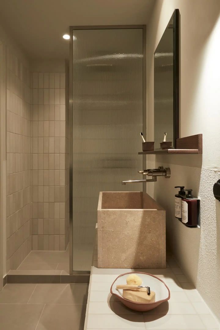 Badezimmer mit eckigem Steinwaschbecken, Wandarmatur und verglaster Dusche.