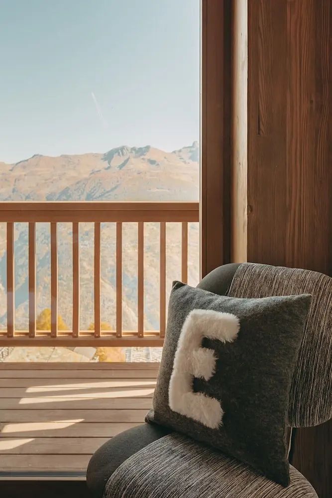 Sessel mit Kissen auf dem Balkon mit Holzgeländer und Blick auf die Berglandschaft.