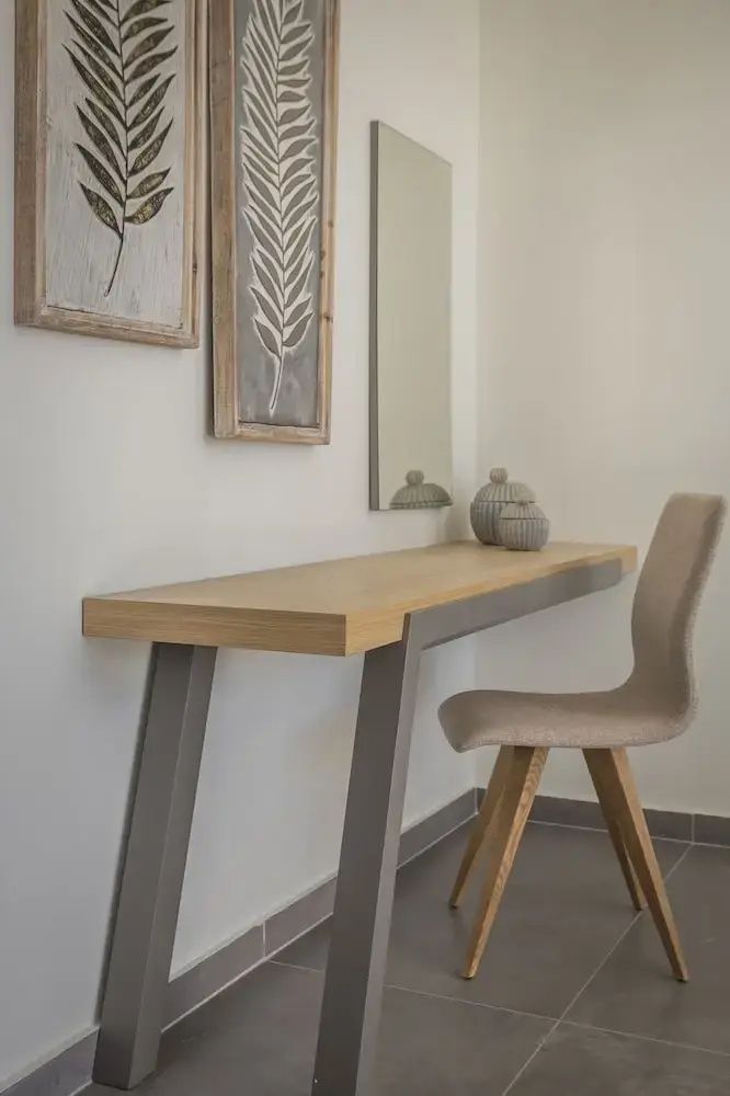 Schreibtisch aus Holz mit einem Polsterstuhl, einem Wandspiegel und zwei Wandbildern.