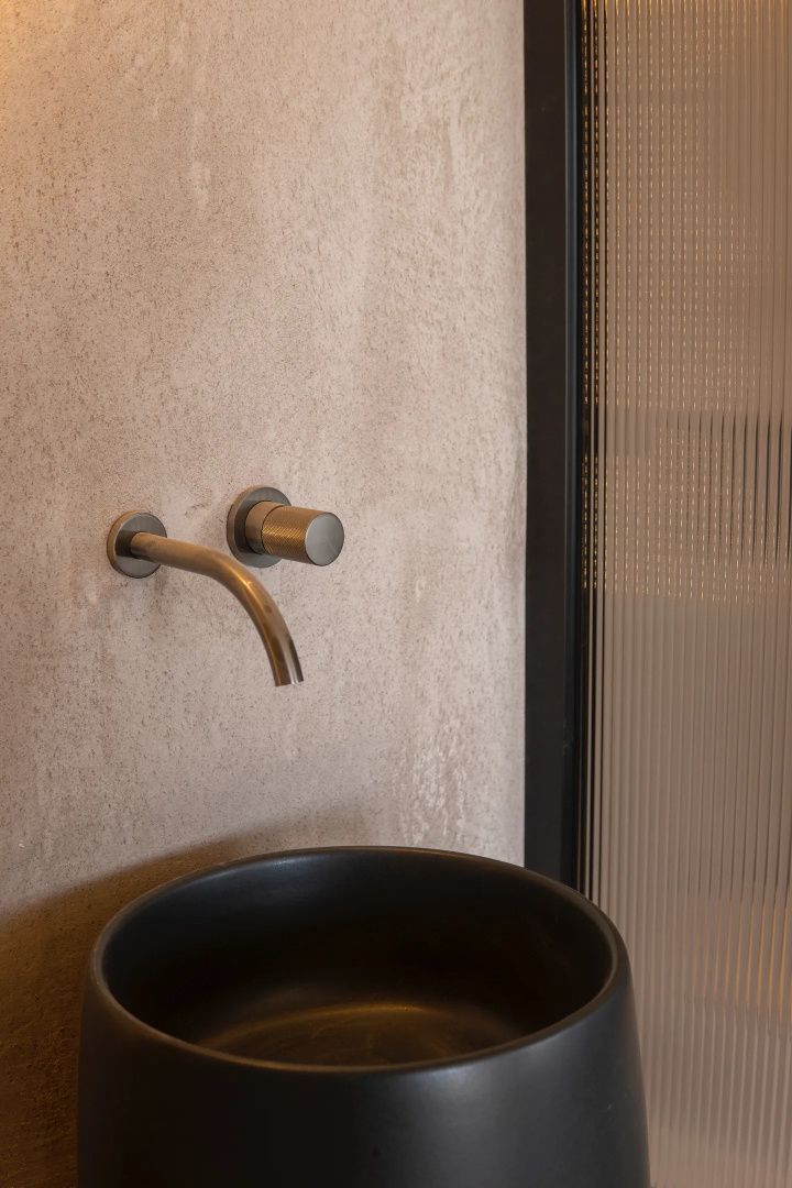 Nahaufnahme einer wandmontierten Metallarmatur über einem schwarzen Waschbecken.