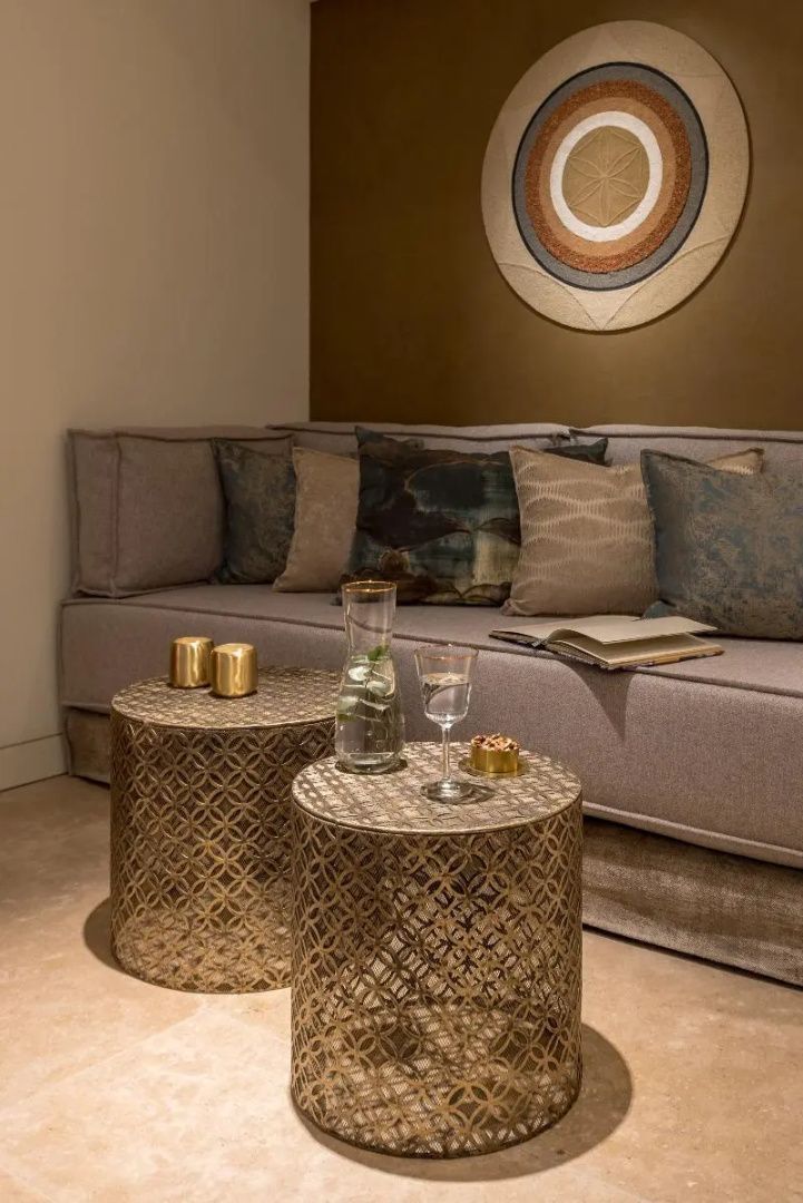 Sitzecke mit grauem Polstersofa, Kissen und zwei metallenen Beistelltischen im Raum.