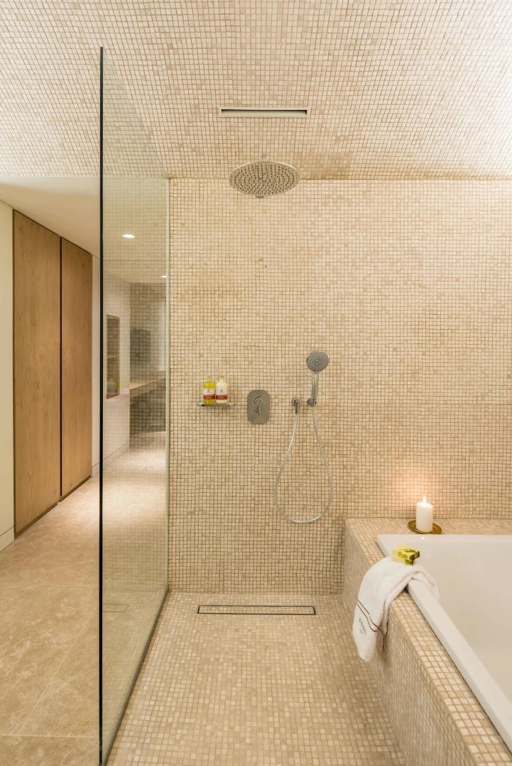 Geflieste begehbare Dusche mit Regenduschkopf und Glastrennwand neben einer Badewanne.