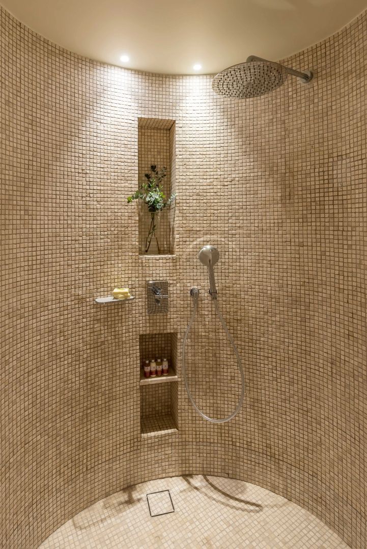 Begehbare Dusche mit beigefarbenen Mosaikfliesen und integrierten Wandnischen.