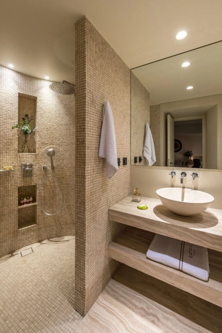 Badezimmer mit Steinwaschtisch, beigefarbener Mosaikdusche und großem Spiegel.