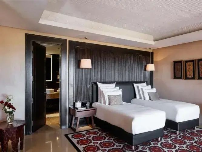 Schlafzimmer mit zwei Einzelbetten, gemustertem Teppich und Blick ins Badezimmer.