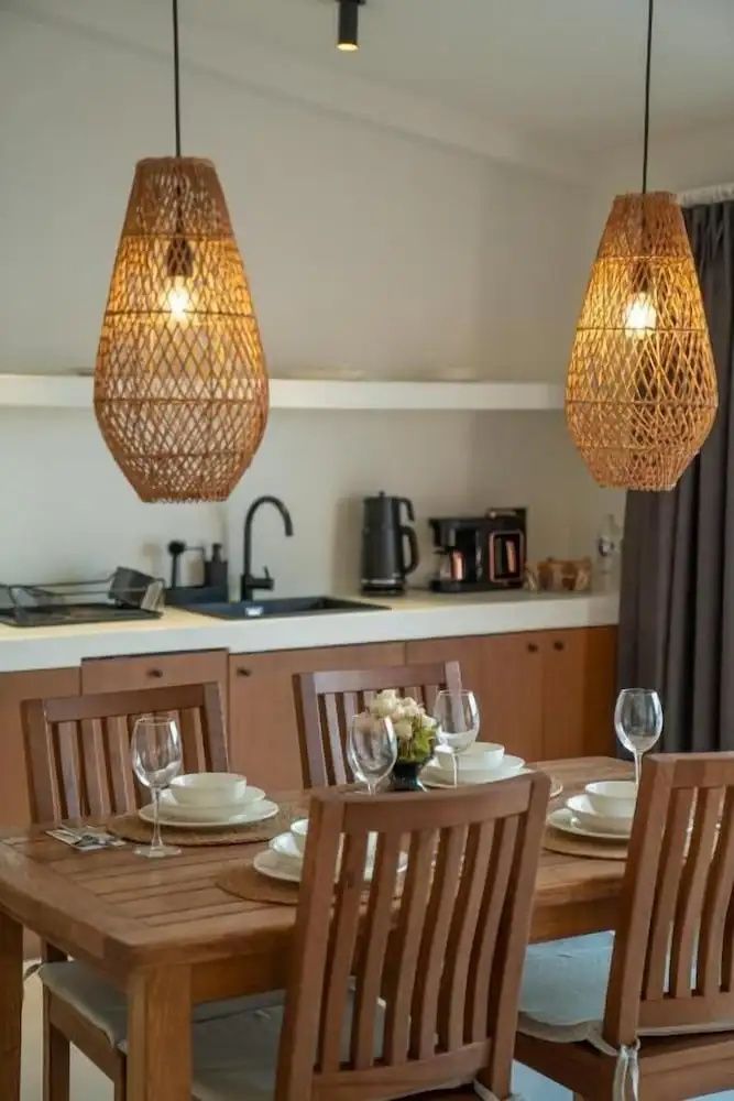 Holztisch mit gedecktem Geschirr und Weingläsern unter zwei geflochtenen Hängelampen in einer modernen Suite.
