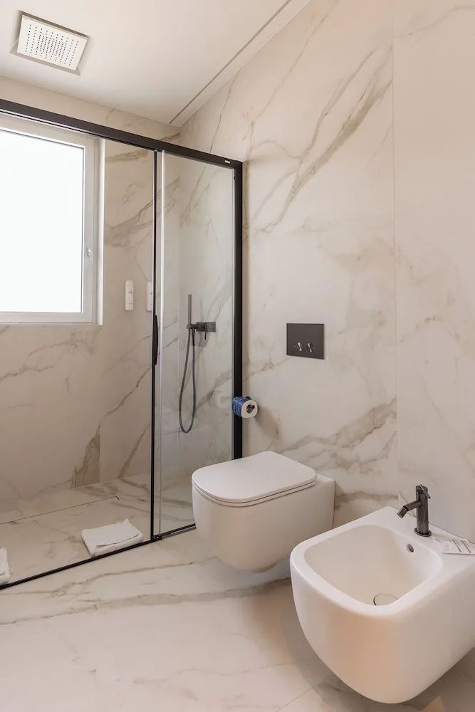 Badezimmer mit weißem Hänge-WC, Bidet und Duschkabine mit schwarzem Rahmen.