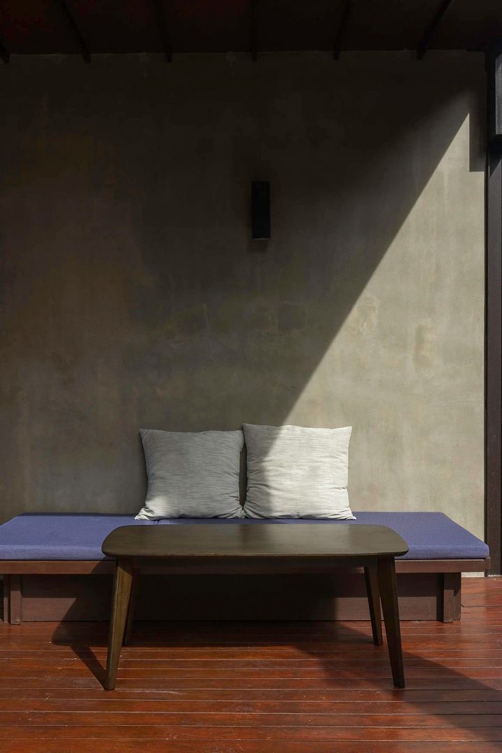 Sitzbank mit blauer Auflage und grauen Kissen vor einer Betonwand auf der Terrasse.