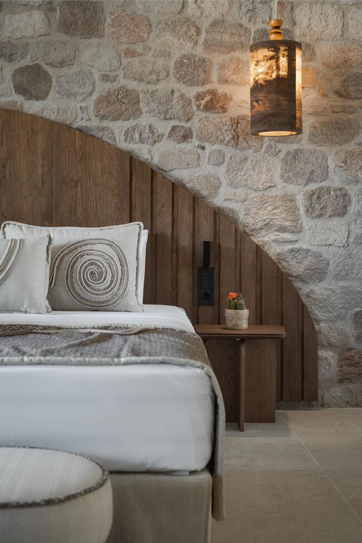 Doppelbett mit verzierten Kissen vor einer Wand aus Naturstein und Holz.