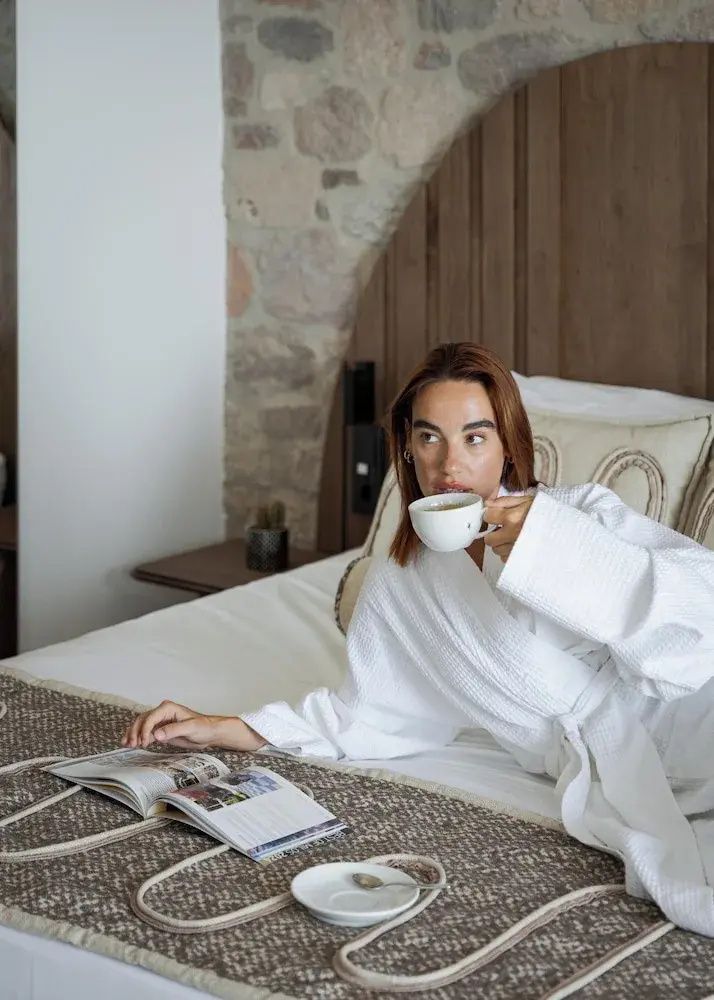 Frau im weißen Bademantel liegt auf dem Bett und liest in einer Zeitschrift.