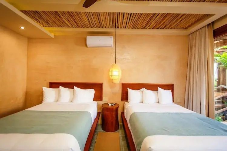 Schlafzimmer mit zwei Doppelbetten, Holzdecke und Wandklimaanlage.