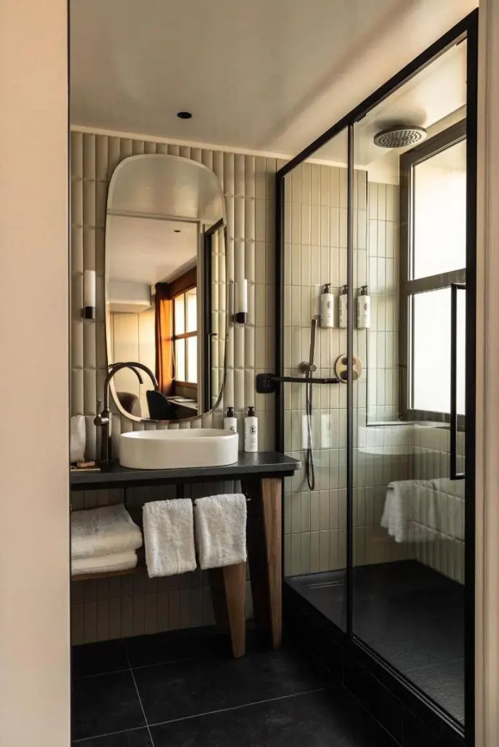 Badezimmer mit ovalem Wandspiegel, weißem Aufsatzwaschbecken und begehbarer Glasdusche.